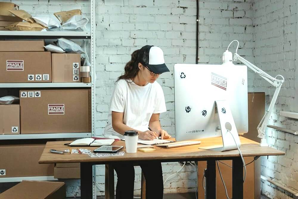 A woman working on fulfilling a customers order with desktop computer.