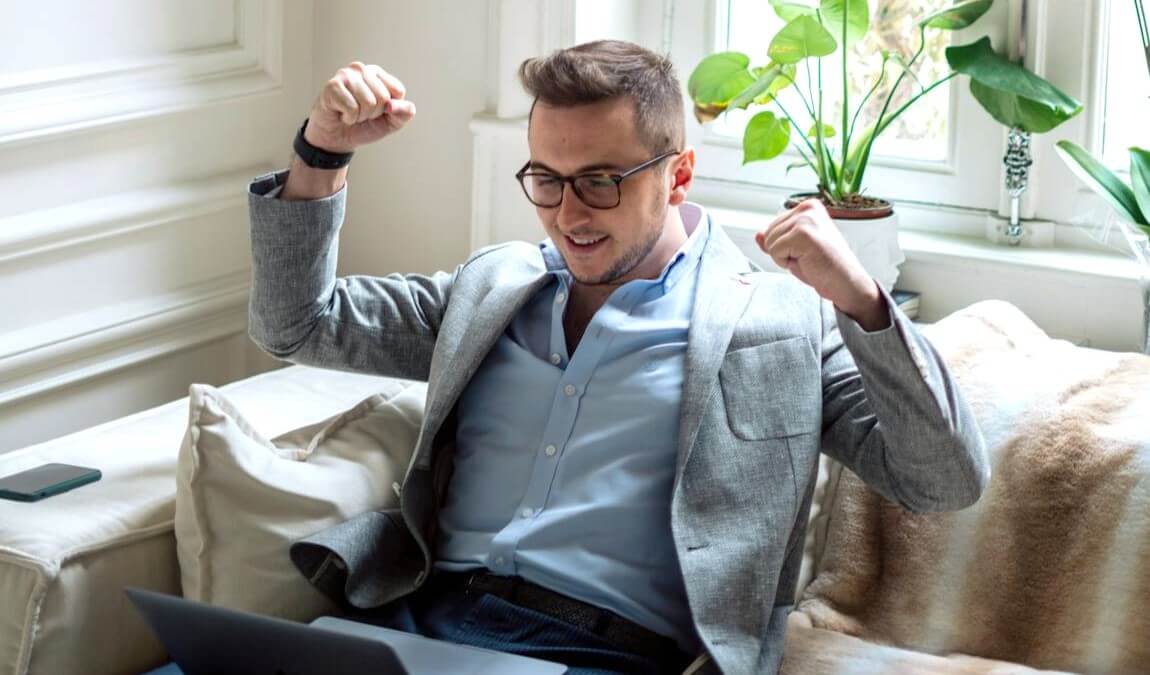 Man cheering while sitting down and looking at laptop